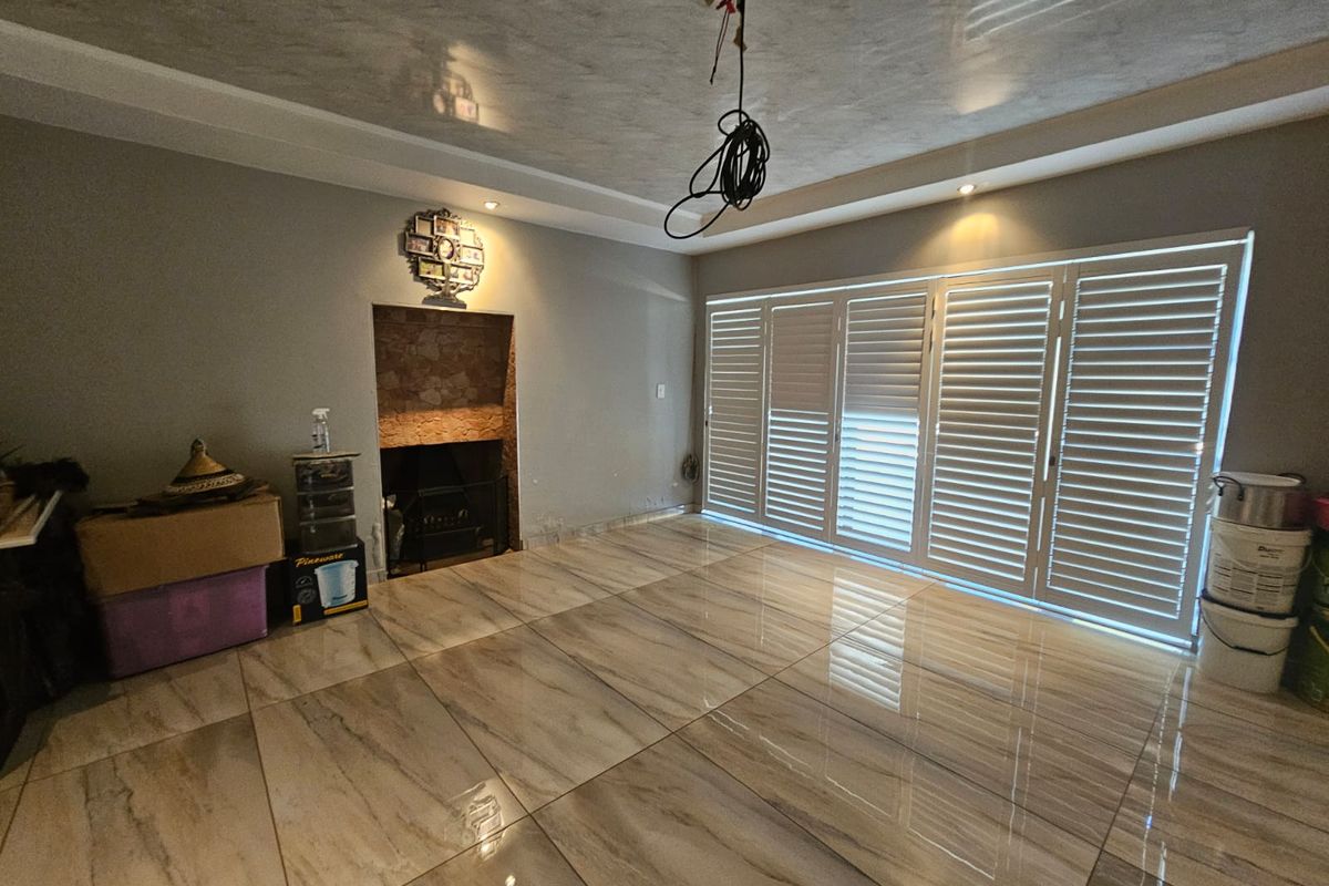 Spacious living room featuring large folding shutter doors, polished tiled flooring, and a stone-accented fireplace, offering a bright and versatile living space.