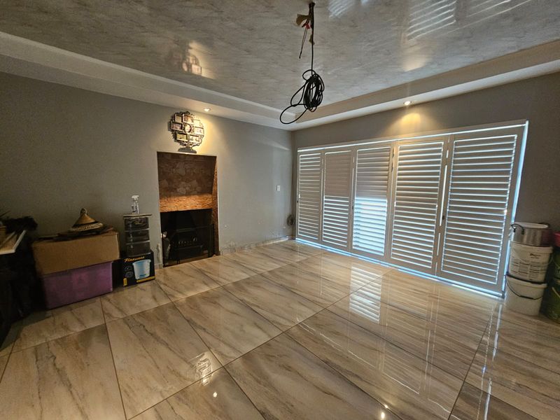 Spacious living room featuring large folding shutter doors, polished tiled flooring, and a stone-accented fireplace, offering a bright and versatile living space.