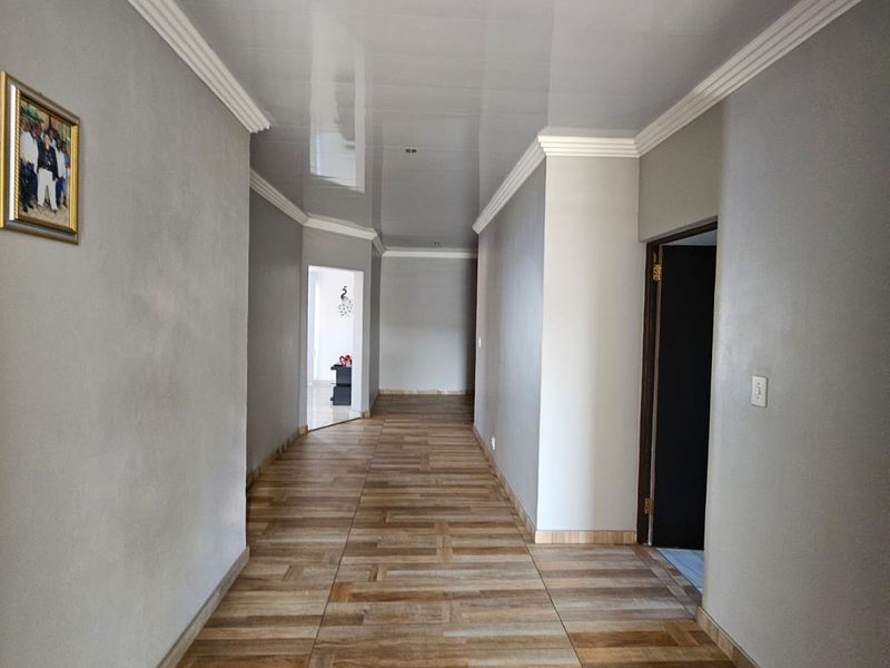A spacious, well-maintained hallway featuring wood-look tiled flooring, glossy ceiling panels, and decorative cornice detailing.