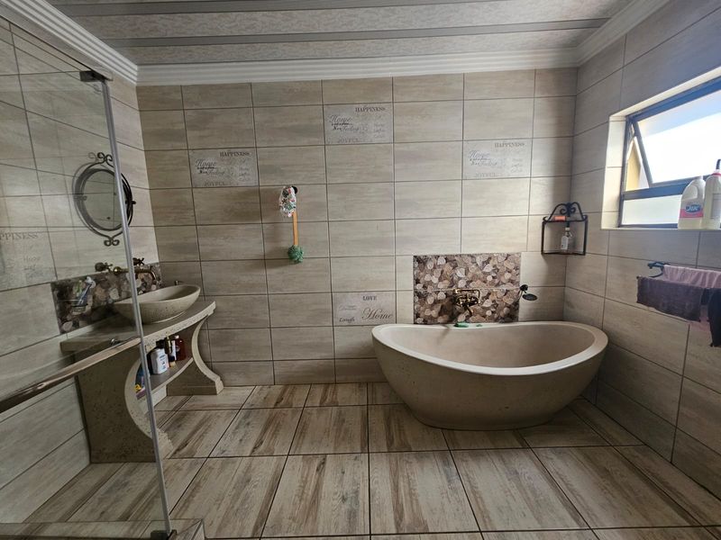 A spacious bathroom featuring a modern freestanding bathtub, a stone-based vessel sink vanity, a glass-enclosed shower, and neutral floor-to-ceiling wall tiling.