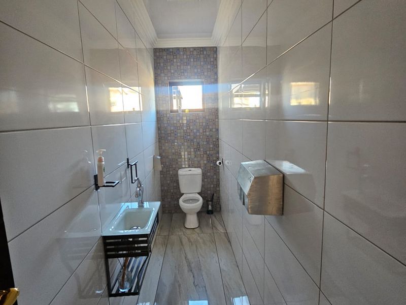 A clean, modern bathroom featuring floor-to-ceiling white wall tiles, marble-effect floor tiles, a wall-mounted basin, and a toilet.