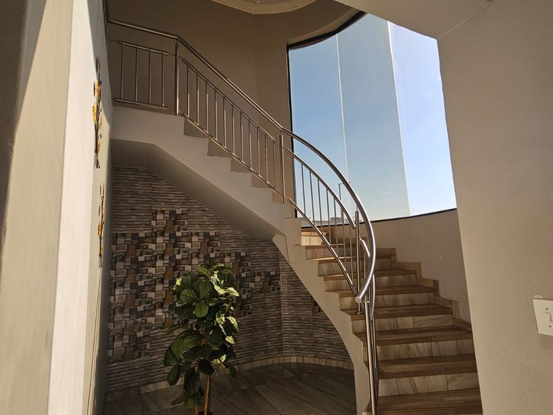 Elegant entrance foyer featuring a striking curved staircase with stainless steel balustrades, tiled flooring, and a decorative stone feature wall.
