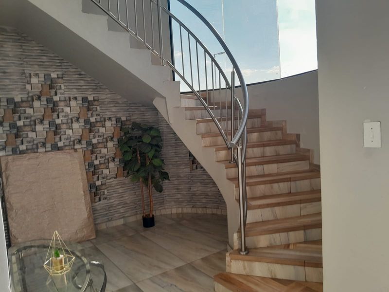An elegant entrance area featuring a curved staircase with a stainless steel balustrade and a decorative stone feature wall.