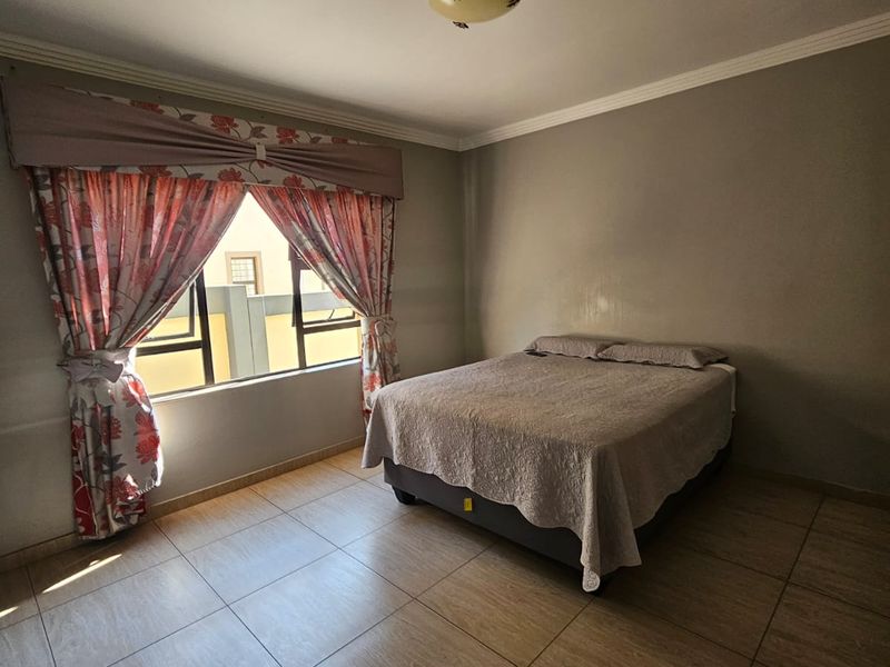 A functional bedroom featuring tiled flooring, a coved ceiling, and a window with security bars, providing a neutral space ready for personalization.
