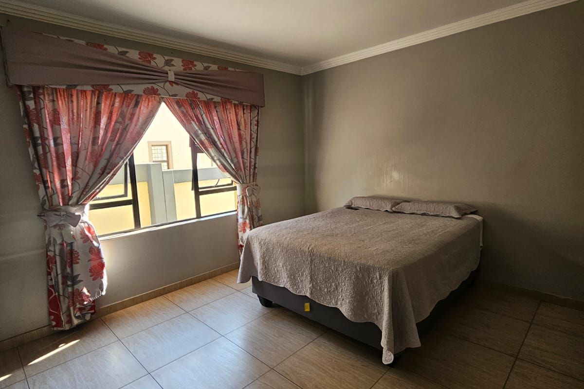 A functional bedroom featuring tiled flooring, a coved ceiling, and a window with security bars, providing a neutral space ready for personalization.