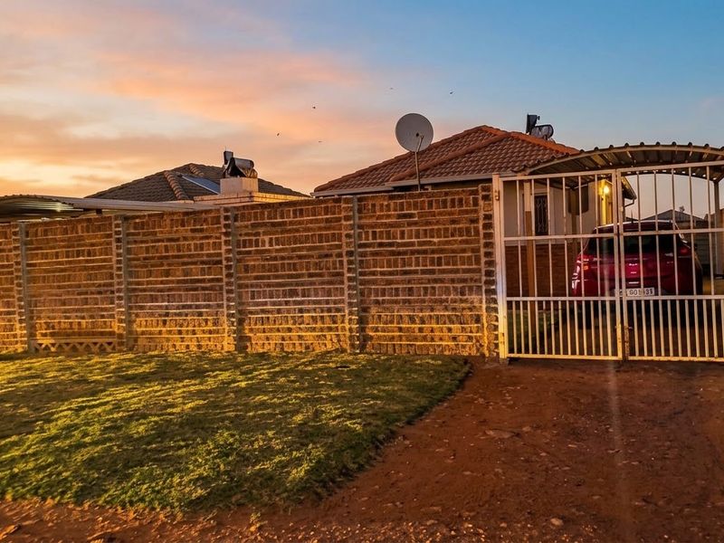 Front exterior view of the property featuring a brick boundary wall, metal driveway gate, and a covered carport area.