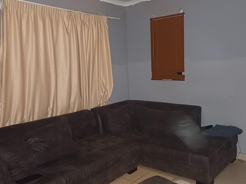 A living room area featuring tiled flooring, grey painted walls, and window treatments including curtains and venetian blinds.