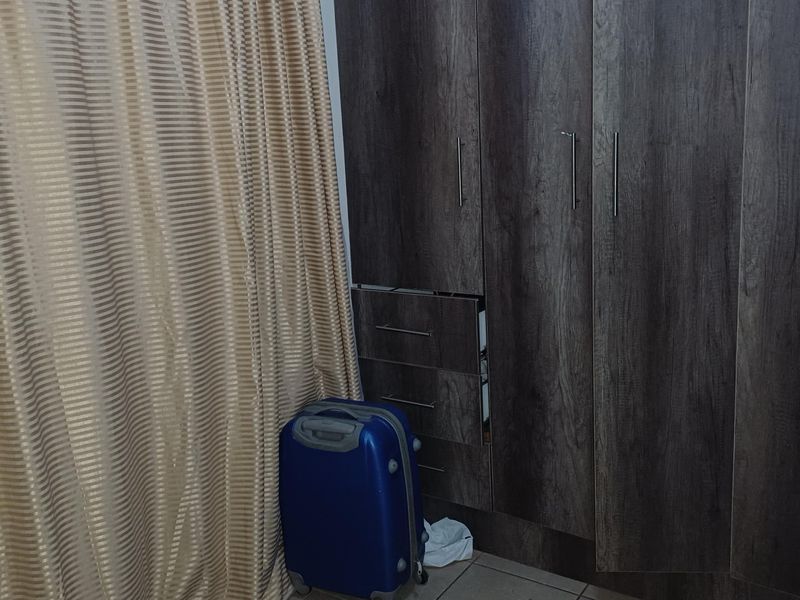 A bedroom featuring dark wood-finish built-in cupboards and tiled flooring.