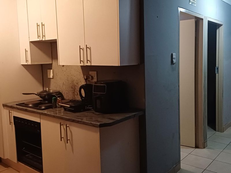 Compact kitchen featuring white cabinetry, laminate countertops, and built-in oven with hob, adjacent to a hallway leading to other rooms.