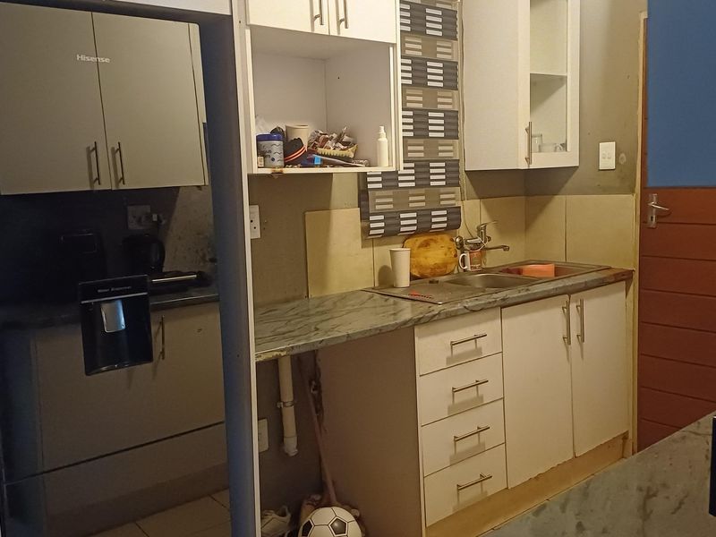 A compact kitchen featuring built-in cabinetry, laminate countertops, and a stainless steel sink, requiring some cosmetic updates to improve functionality and aesthetic appeal.