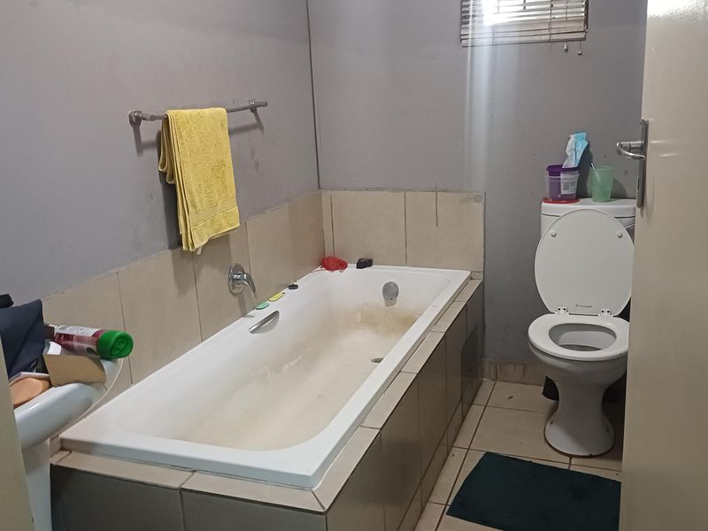 A functional bathroom featuring a built-in bathtub, toilet, and tiled finishes, currently requiring cosmetic updates and maintenance to improve its overall condition.