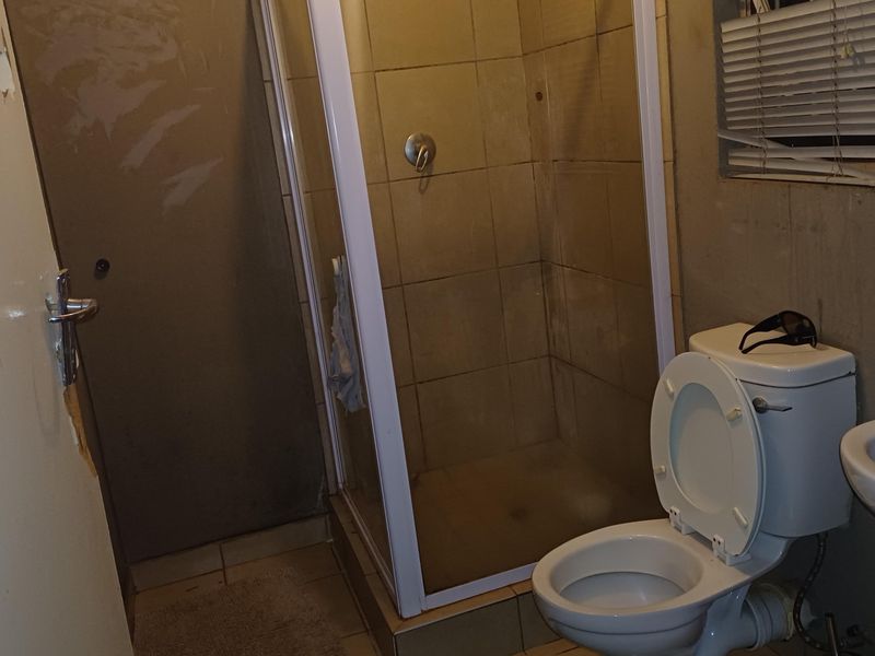 A compact bathroom featuring a shower enclosure, toilet, and basin, currently requiring maintenance and cosmetic updates to improve its overall condition.