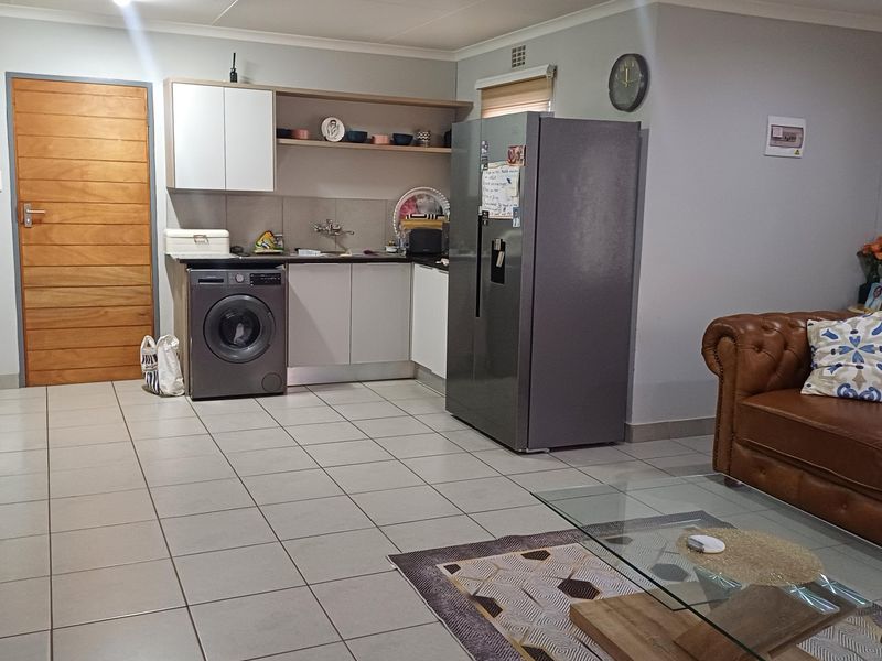 Open plan living area featuring tiled flooring and a compact kitchen corner with built-in cabinetry and laundry plumbing connections.