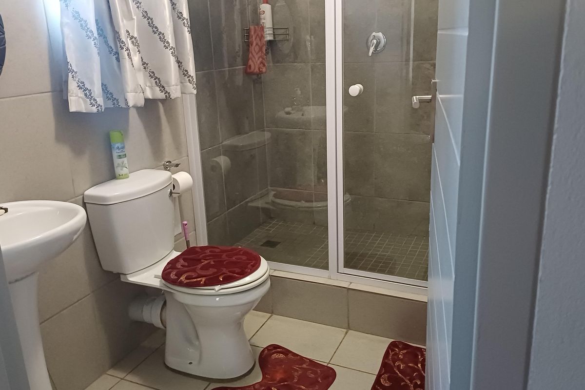 A functional bathroom featuring a pedestal basin, a standard toilet, and a tiled shower enclosure with a glass door.