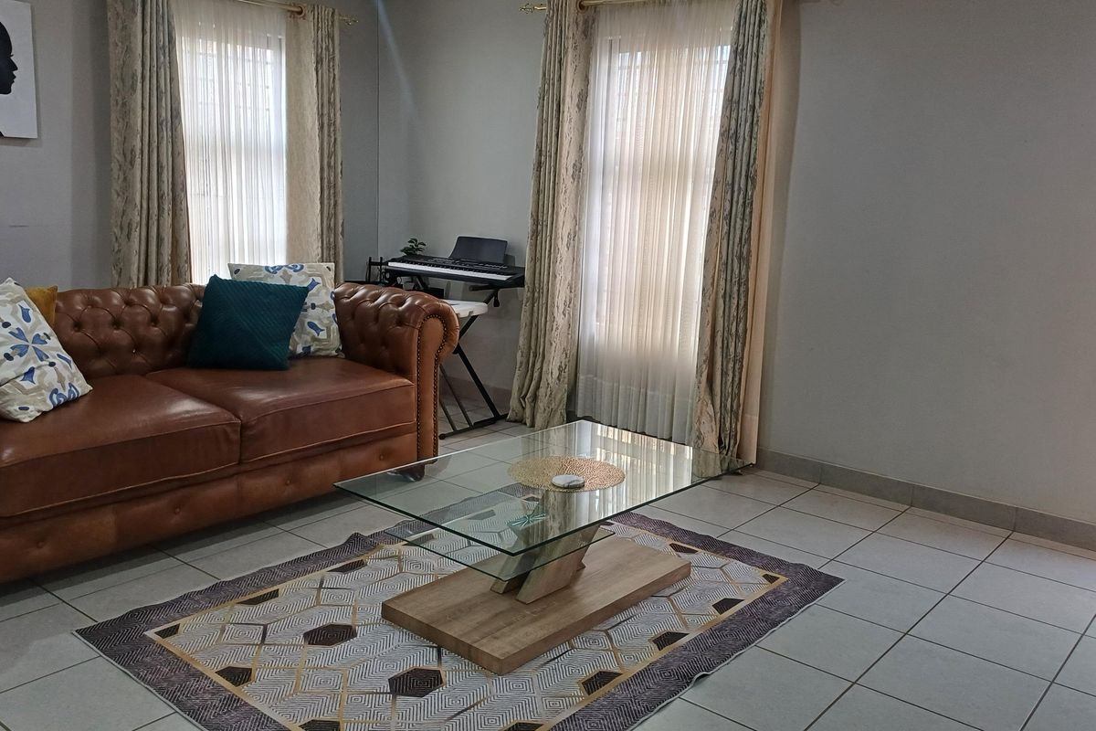 A comfortable living room featuring neutral tiled flooring and dual windows with installed curtain rails, providing a bright and functional space.