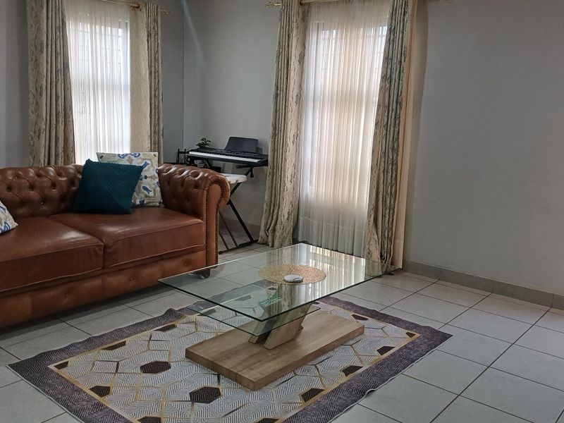 A comfortable living room featuring neutral tiled flooring and dual windows with installed curtain rails, providing a bright and functional space.