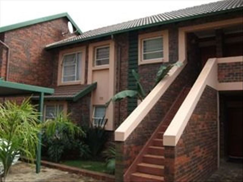 Exterior view of a face brick apartment complex featuring an external staircase, tiled roofing, and a covered carport area.