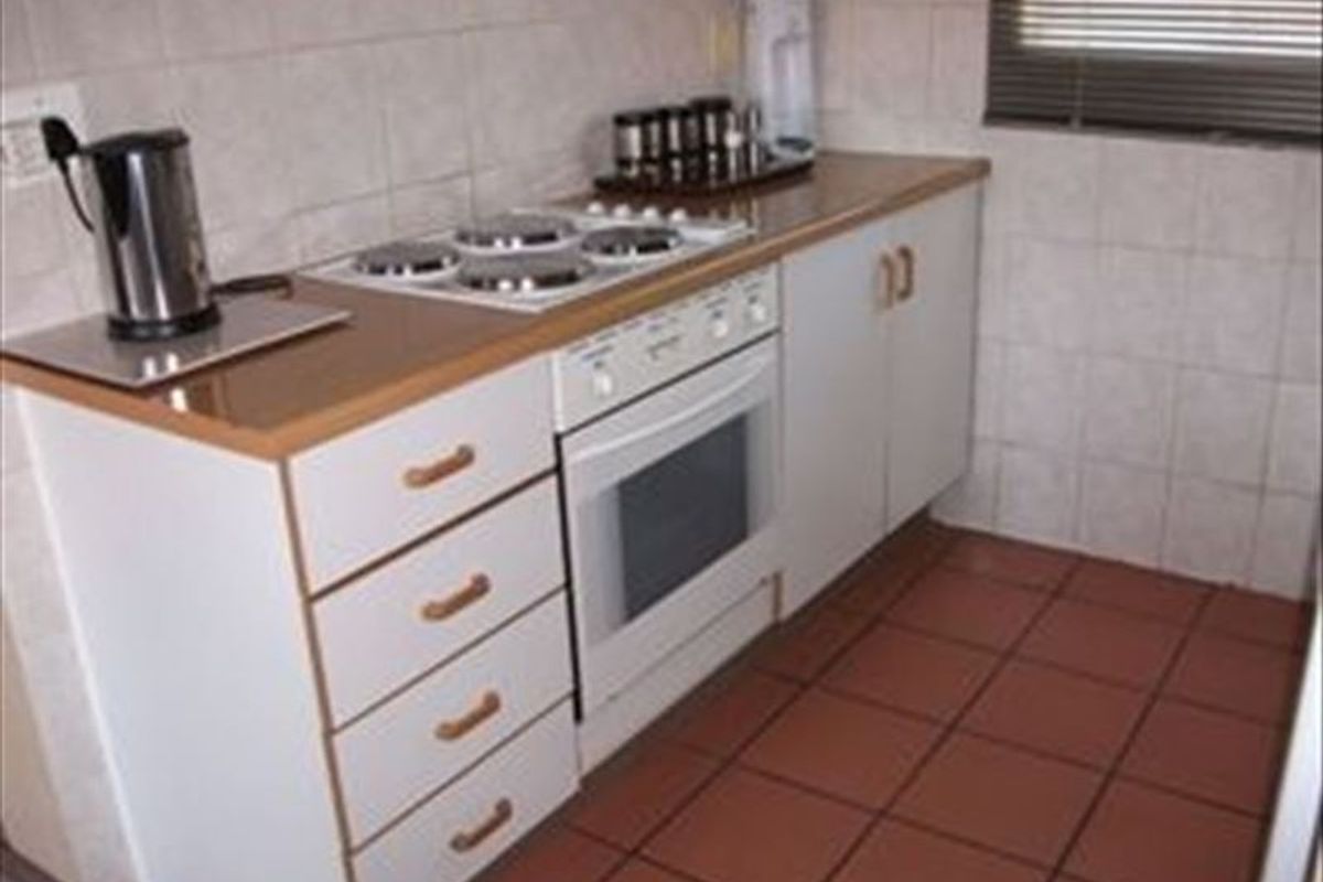 A compact kitchen featuring built-in cabinetry, a laminate countertop, an electric hob, an oven, and tiled finishes throughout.