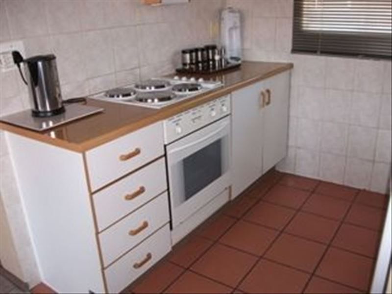 A compact kitchen featuring built-in cabinetry, a laminate countertop, an electric hob, an oven, and tiled finishes throughout.