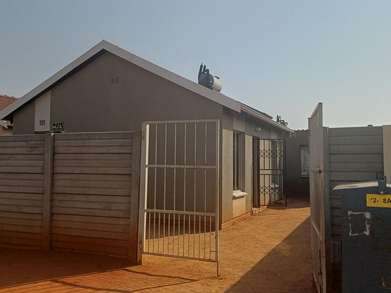 Front view of a residential property featuring a precast concrete boundary wall, metal security gate, and a solar water heater installed on the roof.