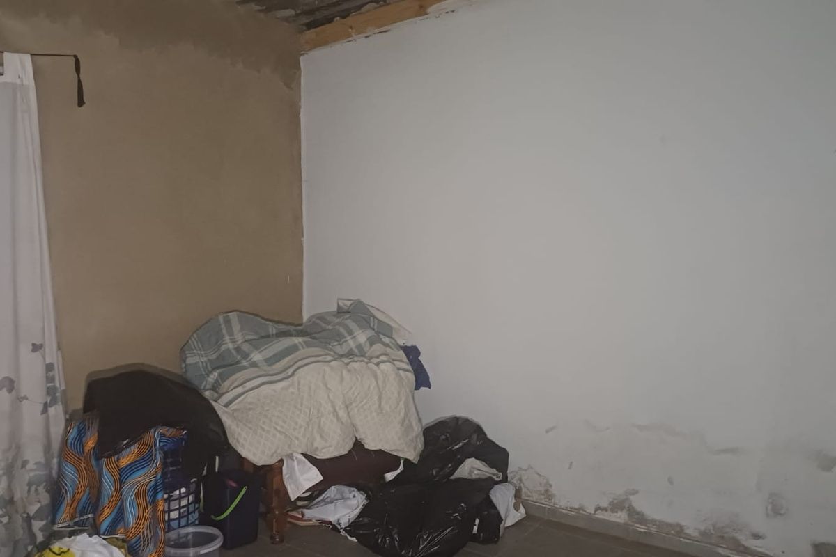 A bedroom space requiring significant renovation, featuring visible rising damp on the lower walls and unfinished ceiling and wall surfaces.