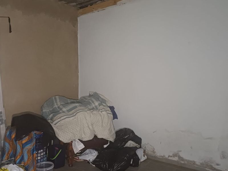 A bedroom space requiring significant renovation, featuring visible rising damp on the lower walls and unfinished ceiling and wall surfaces.