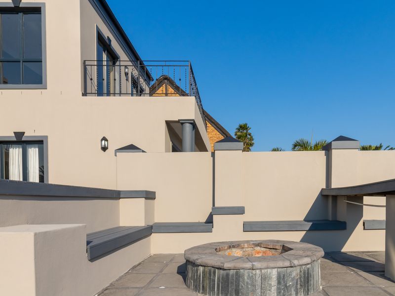 A well-maintained outdoor patio area featuring a stone-built fire pit, integrated bench seating, and a balcony overlooking the space.