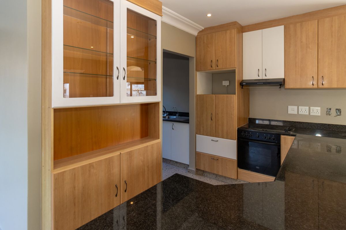 A well-maintained kitchen featuring granite countertops, built-in oven, extractor fan, and a mix of wood-finish and white cabinetry with glass display sections.