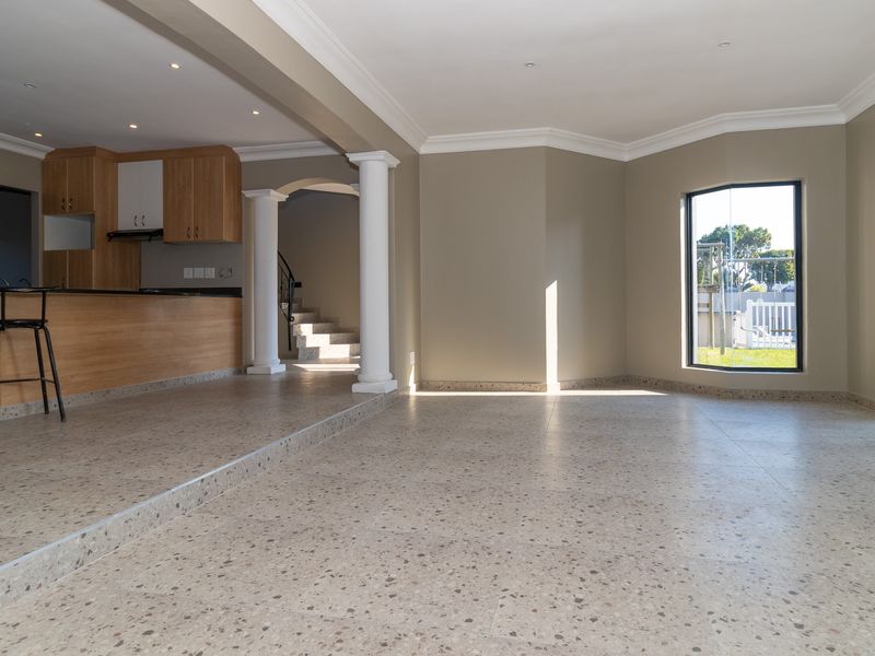 Spacious open-plan living and kitchen area featuring terrazzo flooring, decorative columns, and abundant natural light through large windows and sliding doors.