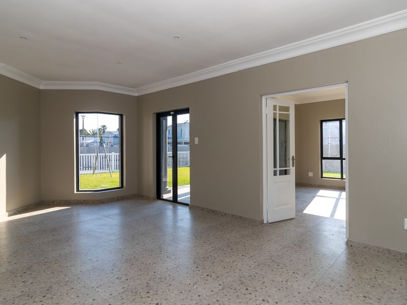A bright, empty living room featuring neutral walls, crown molding, terrazzo-style flooring, and direct access to the garden through a sliding glass door.
