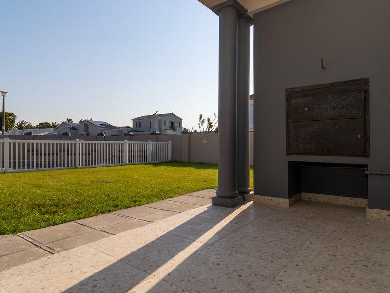 Covered patio area featuring a built-in braai, terrazzo-style flooring, and structural columns, overlooking a private garden with a white picket fence.
