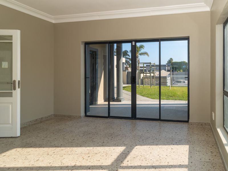 Bright and spacious living area featuring terrazzo flooring, large sliding glass doors leading to the garden, and a classic white french door.