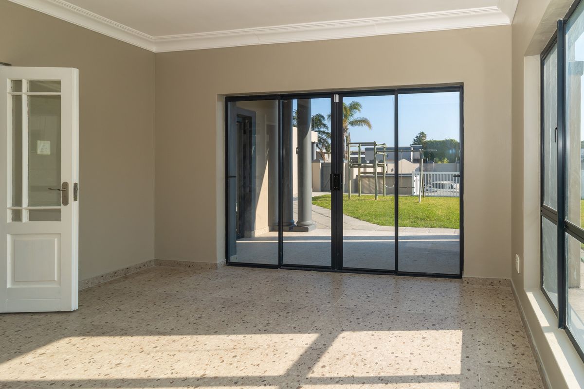 Bright and spacious living area featuring terrazzo flooring, large sliding glass doors leading to the garden, and a classic white french door.