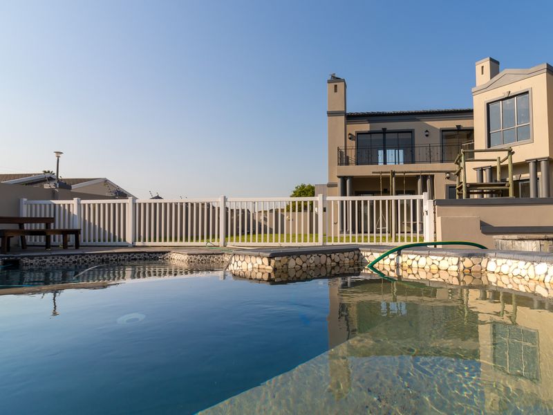 A well-maintained swimming pool area featuring stone-clad coping, a white perimeter fence, and a view of the multi-story residential building exterior.