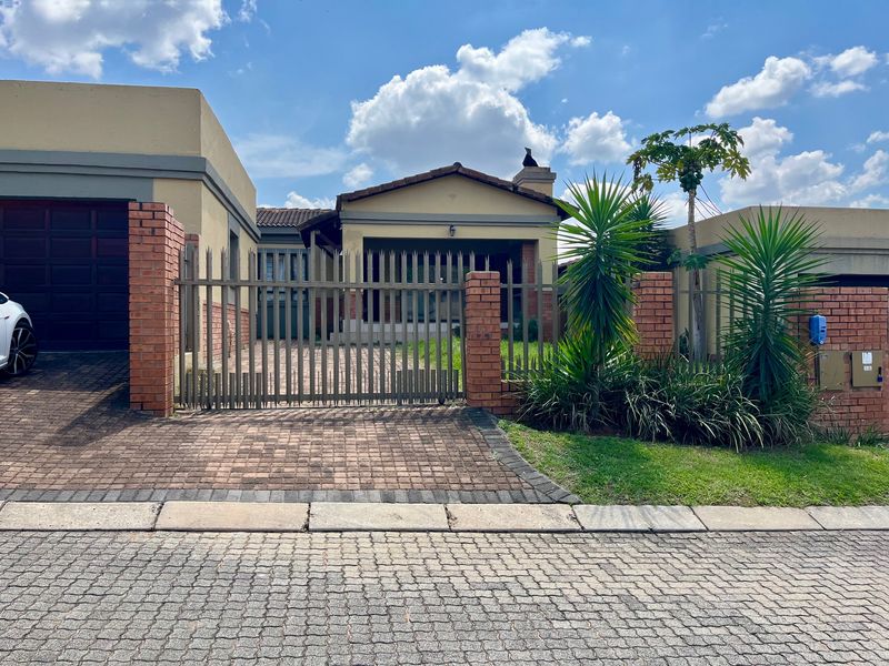 Front elevation of a residential house featuring a paved driveway, metal security gate, brick pillars, and a tiled roof.