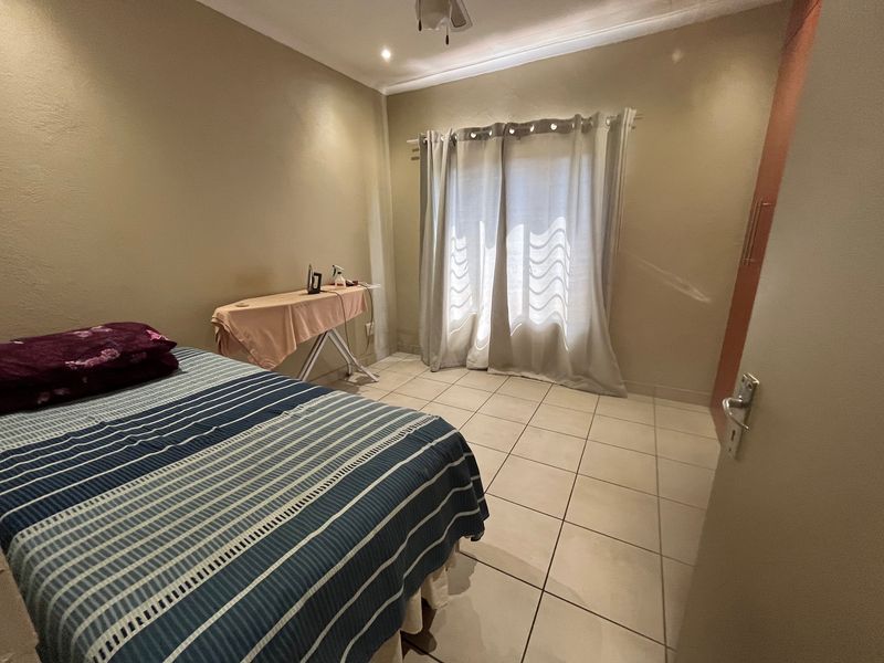 A functional bedroom featuring tiled flooring, a built-in cupboard, and natural light through a window with curtain fittings.