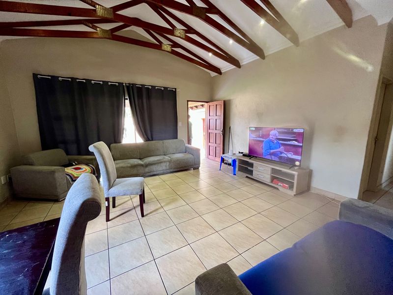 Spacious living room featuring high vaulted ceilings with exposed timber beams and neutral tiled flooring, offering a comfortable and open living environment.