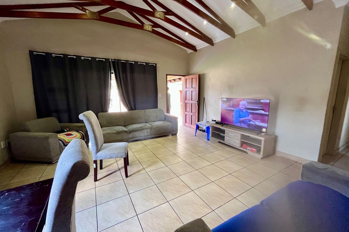 Spacious living room featuring high vaulted ceilings with exposed timber beams and neutral tiled flooring, offering a comfortable and open living environment.