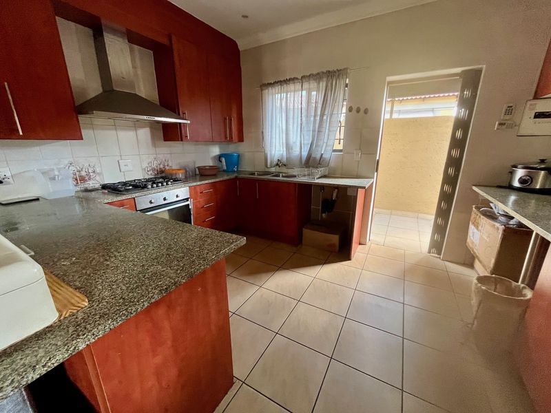 Functional kitchen featuring wood-finish cabinetry, granite countertops, gas hob, and tiled flooring, with direct access to an outdoor area.