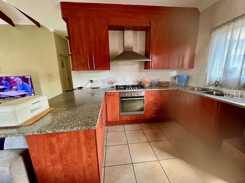 A functional kitchen featuring wooden cabinetry, granite countertops, a built-in oven with gas hob, and a stainless steel extractor fan.
