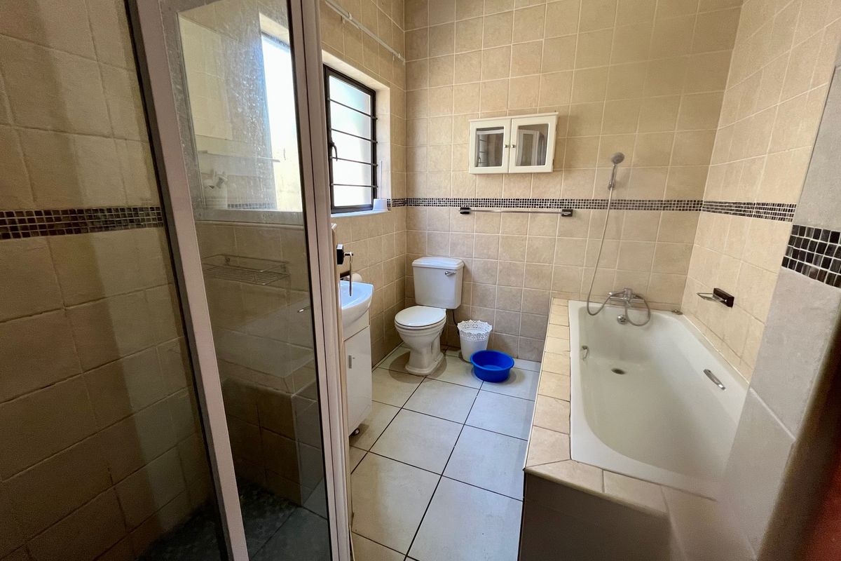 A functional bathroom featuring a bathtub, separate shower enclosure, toilet, and vanity basin with neutral wall and floor tiling.