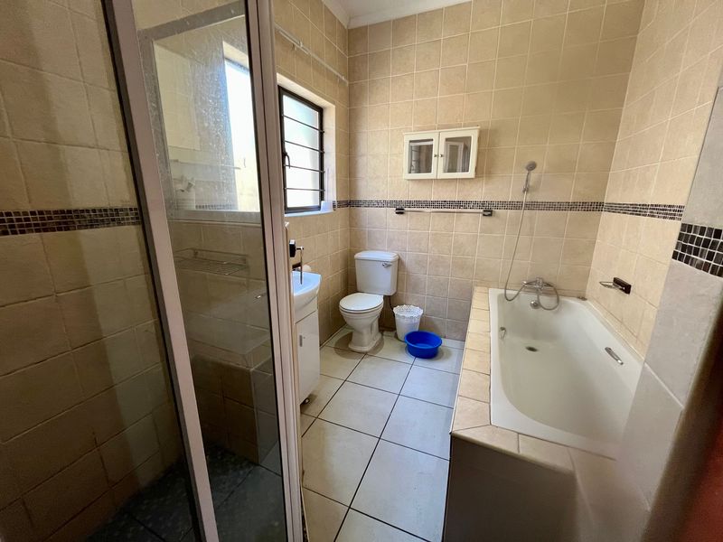 A functional bathroom featuring a bathtub, separate shower enclosure, toilet, and vanity basin with neutral wall and floor tiling.