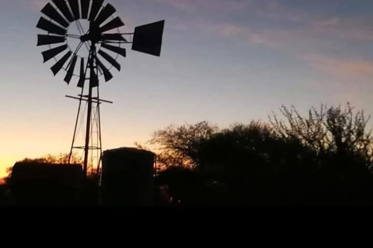 A silhouette view of a traditional farm windmill and water tank against a sunset sky.