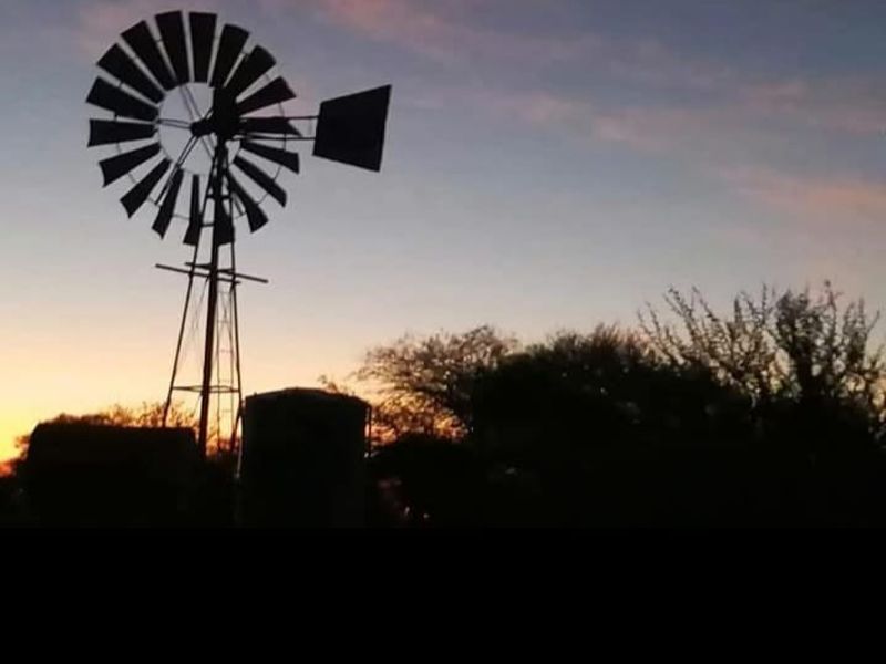 A silhouette view of a traditional farm windmill and water tank against a sunset sky.