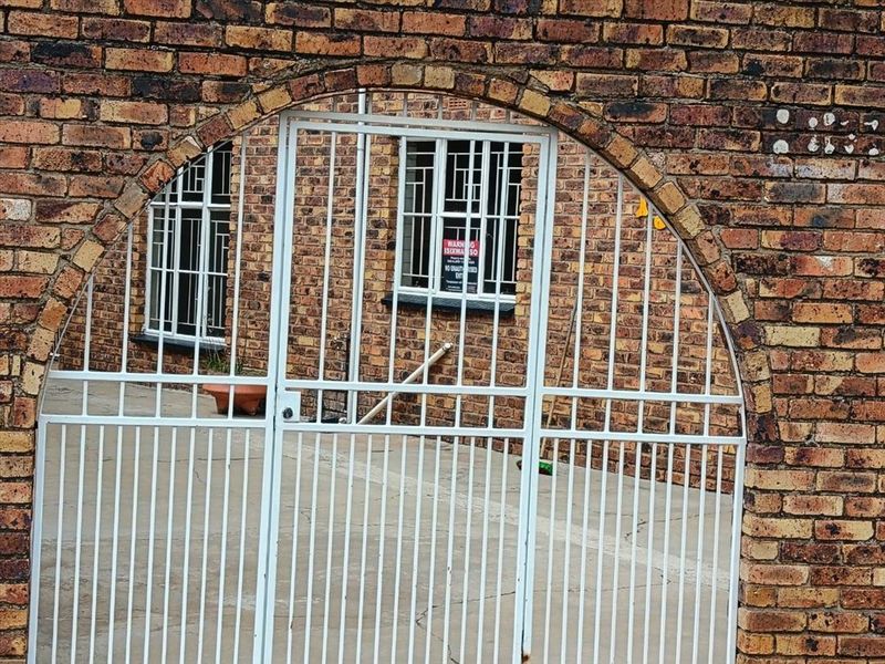 A view of a brick apartment building exterior featuring a white metal security gate and security bars on the windows.