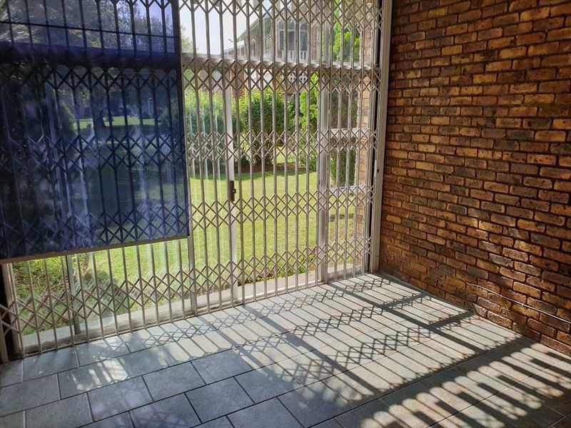 A covered patio area featuring exposed brick walls, tiled flooring, and a security gate, providing direct access to the garden.