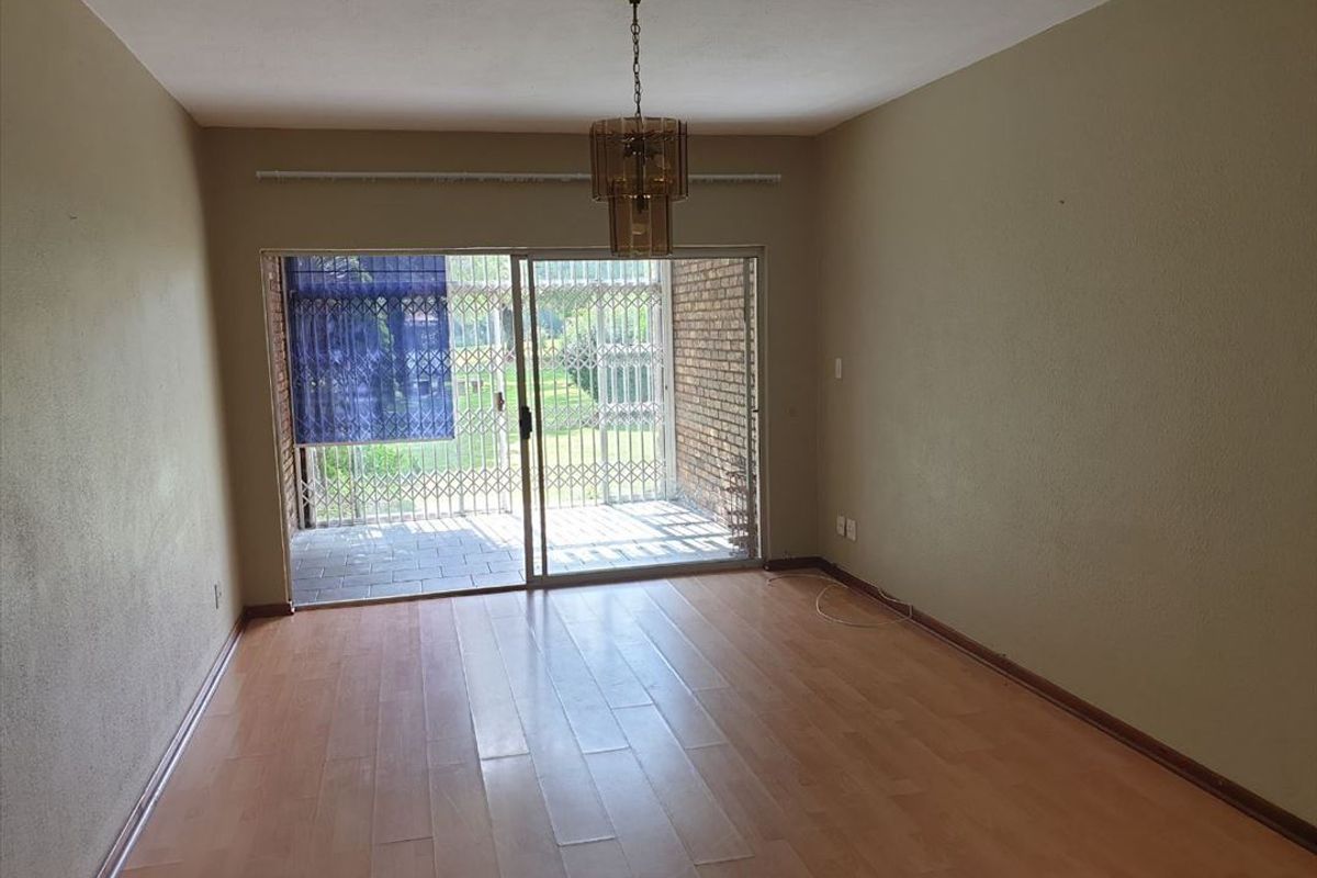 An empty living room featuring laminate flooring, a pendant light, and a sliding glass door leading to an outdoor patio area with security gates.