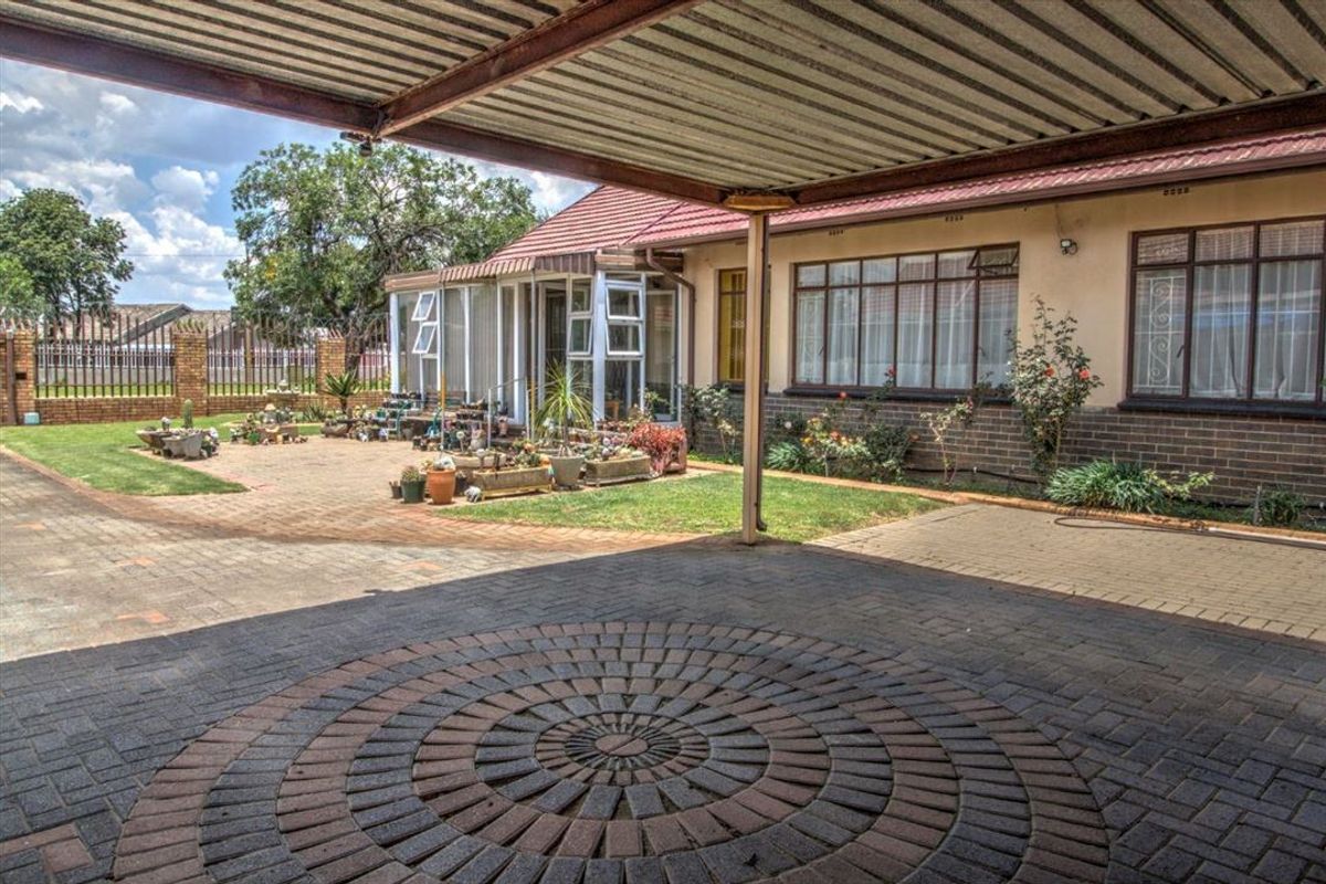 Rear exterior view featuring a paved driveway, a covered carport, and an enclosed patio area with brick and plaster finishes.
