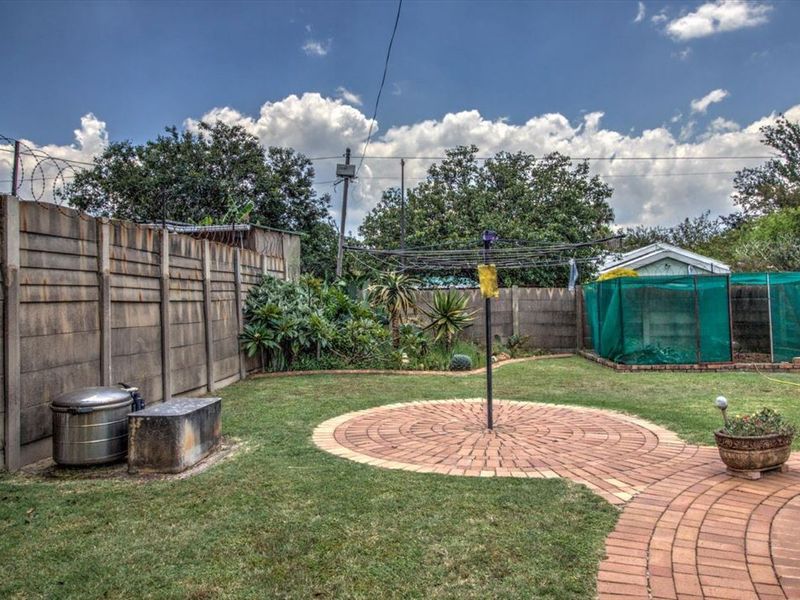 A private rear garden featuring a lawn, circular brick paved area, and precast concrete boundary walls with security razor wire.