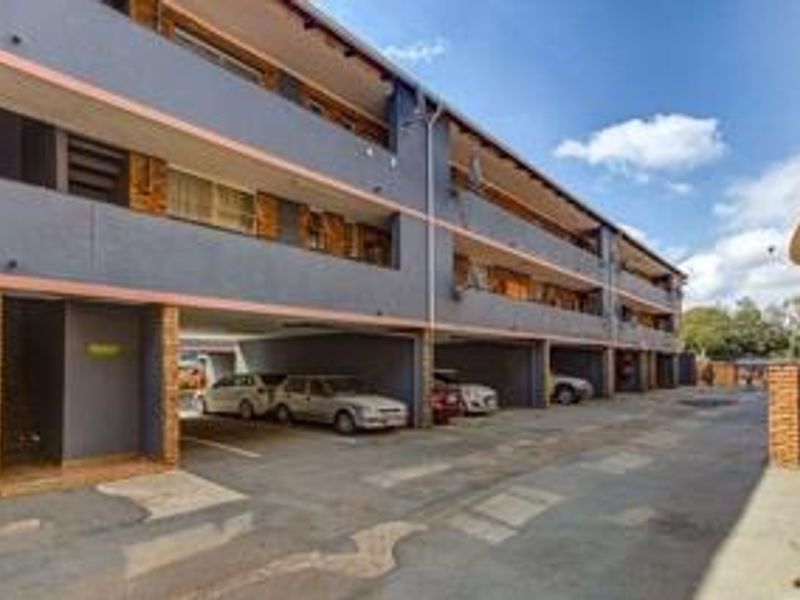 Exterior view of an apartment complex featuring covered ground-level parking bays and multi-story residential units with balconies.